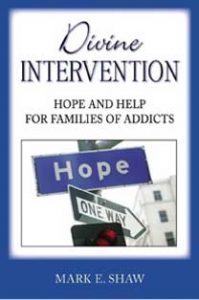 blue and white cover Divine Intervention Hope and Help for Families of Addicts Hope by Mark E. Shaw with street sign on top of One Way street sign in city block with traffic light and building